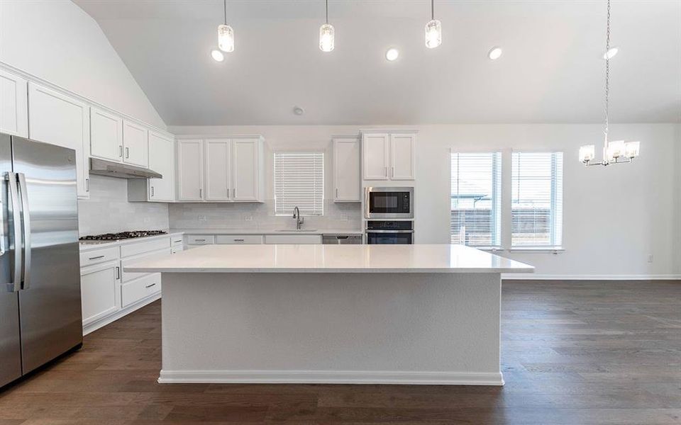 Open-concept kitchen with a large island featuring a light-toned countertop, white cabinetry, and stainless steel appliances