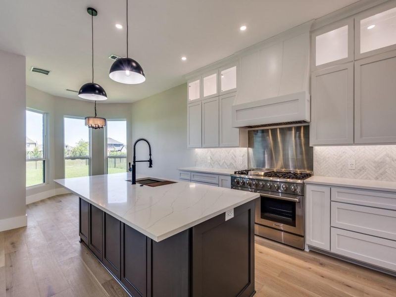 Kitchen featuring high end stainless steel range, a sink, a kitchen island with sink, decorative backsplash, and recessed lighting