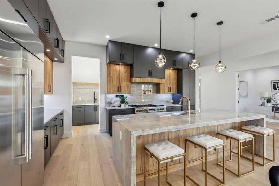 Kitchen featuring a kitchen bar, light stone counters, high end refrigerator, hanging light fixtures, and a kitchen island with sink