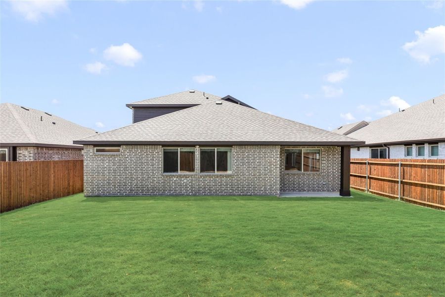 Rear view of brick home with large green backyard and wood privacy fence on both sides