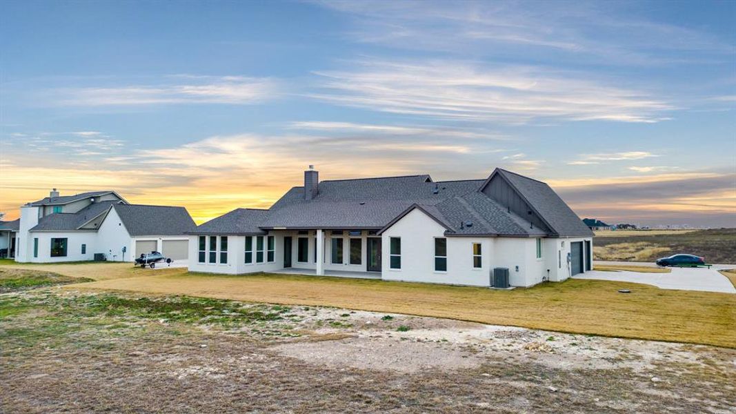 Back house at dusk featuring a lawn and central AC