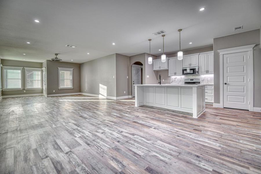 Kitchen featuring arched walkways, open floor plan, white cabinets, a kitchen island with sink, and recessed lighting
