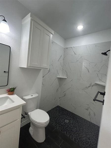 Bathroom with toilet, vanity, and tiled shower