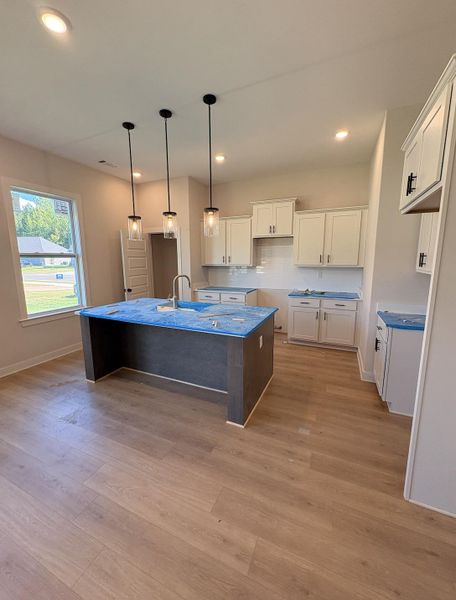Kitchen featuring a central island, recessed lighting, wood-finish flooring, white cabinetry with dark hardware, and a subway tile backsplash Kitchen featuring a central island, recessed lighting, wood-finish flooring, white cabinetry with dark hardware, and a subway tile backsplash
