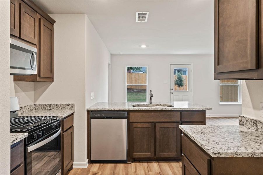 Kitchen featuring light stone counters, sink, light wood-type flooring, and appliances with stainless steel finishes