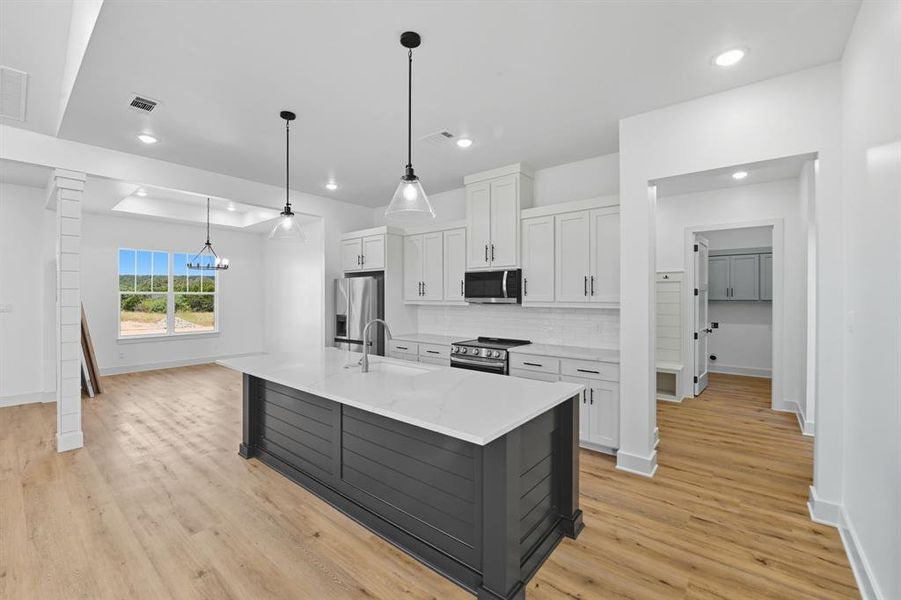 Kitchen featuring white cabinets, tasteful backsplash, hanging light fixtures, an island with sink, and light wood-type flooring Kitchen featuring white cabinets, tasteful backsplash, hanging light fixtures, an island with sink, and light wood-type flooring
