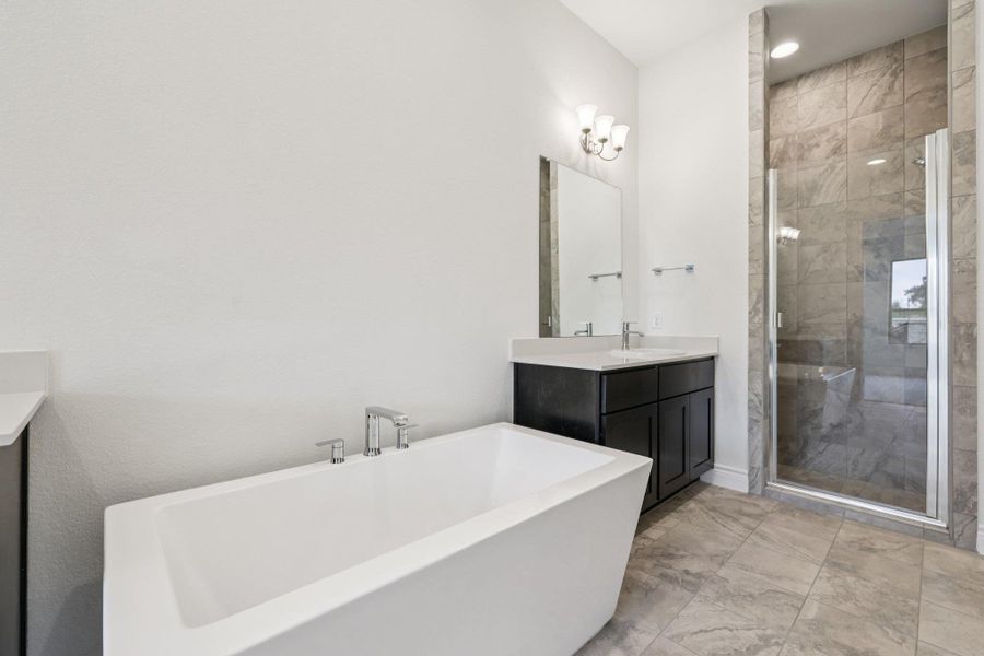 Full bath with vanity, a freestanding bath, a shower stall, and light marble finish floors
