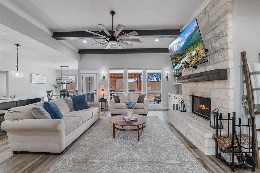 Living room featuring hardwood / wood-style flooring, ceiling fan, a stone fireplace, and beamed ceiling