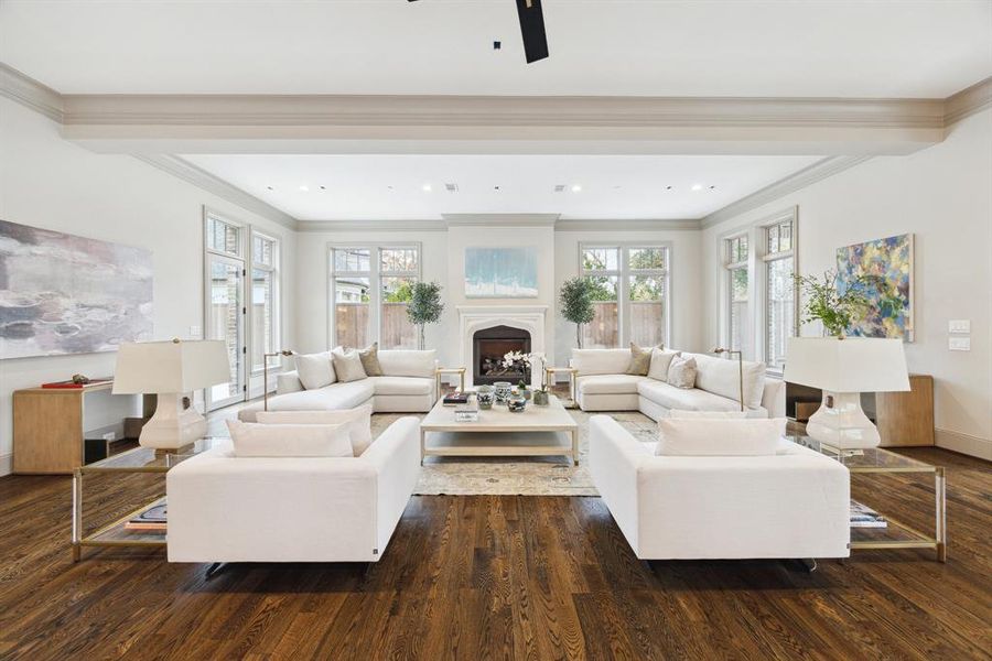 The inviting living room features soaring ceilings with elegant beams, a stately fireplace as the focal point, and walls of windows that fill the space with natural light. The thoughtful layout is ideal for both relaxing and entertaining, with direct access to the outdoor areas through multiple doors. The warm hardwood floors add richness and timeless appeal.