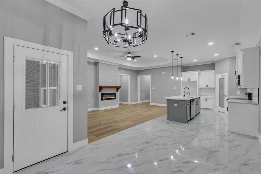 Kitchen with a kitchen island with sink, sink, hanging light fixtures, ornamental molding, and white cabinetry