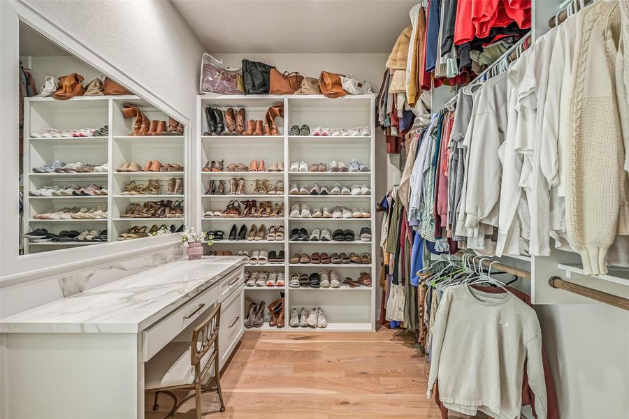 One of two customized primary closets offers extensive hanging space, built-in drawers and an impressive wall of dedicated shoe shelving, plus a vanity/dressing station with additional storage and countertop space.