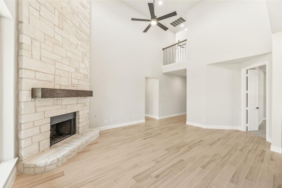 Open living room with floor-to-ceiling stone fireplace, high vaulted ceiling, ceiling fan, and light wood-look tile floors Open living room with floor-to-ceiling stone fireplace, high vaulted ceiling, ceiling fan, and light wood-look tile floors