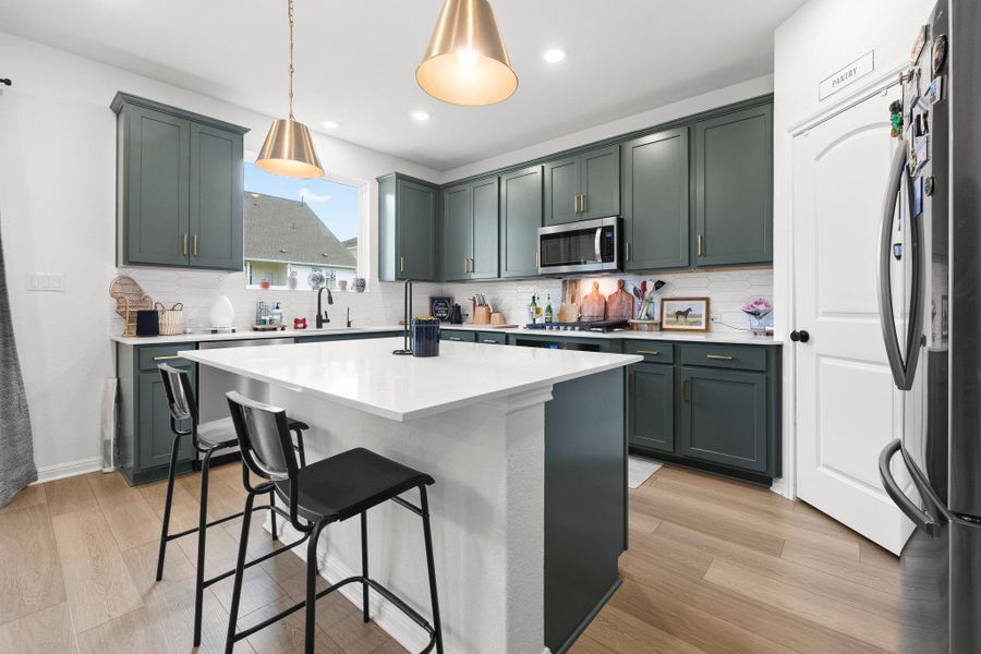 Contemporary kitchen featuring a large central island, dark green cabinetry, white countertops, stainless steel appliances, and wood-finish flooring