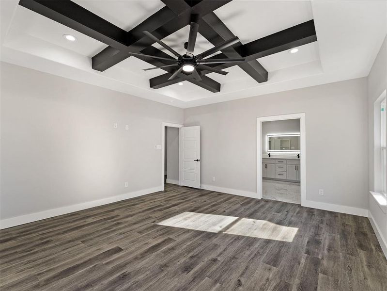 Unfurnished bedroom featuring beam ceiling, ensuite bath, ceiling fan, dark wood-type flooring, and coffered ceiling