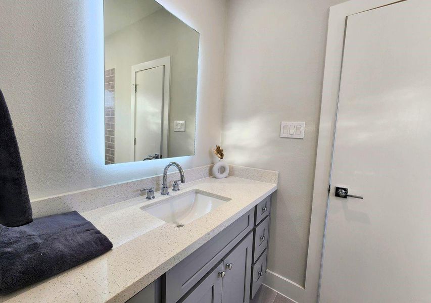 This photo shows a modern bathroom with a sleek vanity featuring a quartz countertop, under-mount sink, and polished chrome faucet. The large mirror and neutral color palette enhance the space, providing a clean and contemporary feel. This photo shows a modern bathroom with a sleek vanity featuring a quartz countertop, under-mount sink, and polished chrome faucet. The large mirror and neutral color palette enhance the space, providing a clean and contemporary feel.