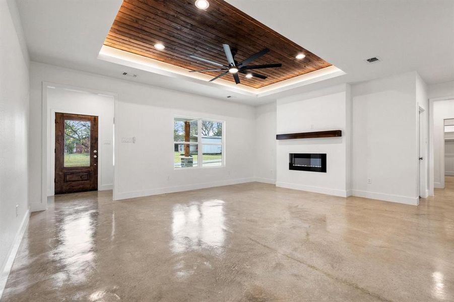 Unfurnished living room with wooden ceiling, a glass covered fireplace, finished concrete floors, a tray ceiling, and ceiling fan