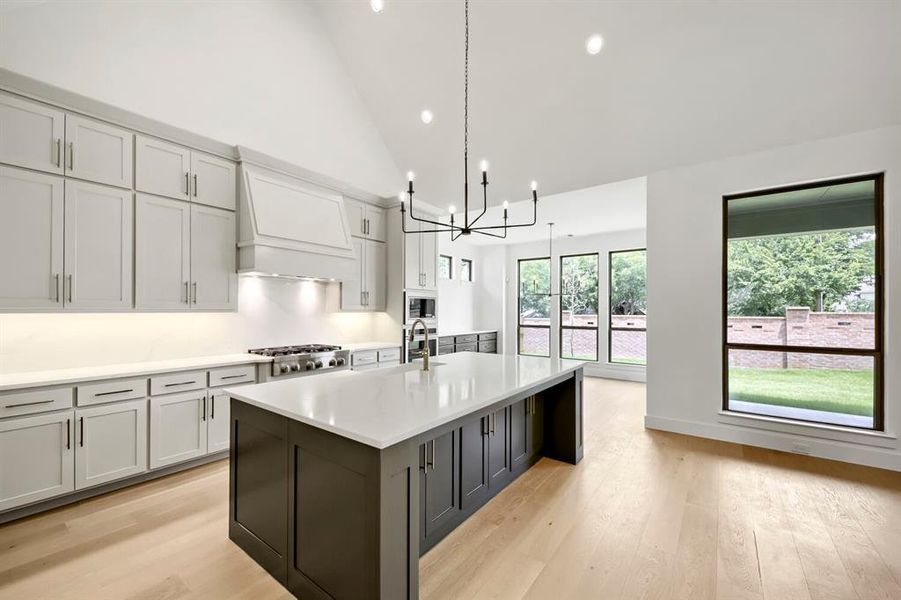 Spacious kitchen featuring an expansive central island with a solid surface countertop, light-toned perimeter cabinetry, a stainless steel gas range, and wood-finish flooring Spacious kitchen featuring an expansive central island with a solid surface countertop, light-toned perimeter cabinetry, a stainless steel gas range, and wood-finish flooring