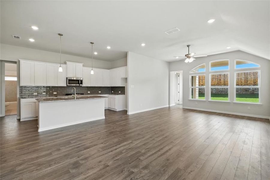 Kitchen featuring stainless steel microwave, open floor plan, a ceiling fan, backsplash, and a center island with sink