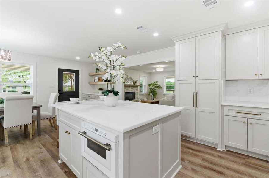 This kitchen features white cabinetry, a large kitchen island with a built-in microwave, and wood-look flooring This kitchen features white cabinetry, a large kitchen island with a built-in microwave, and wood-look flooring