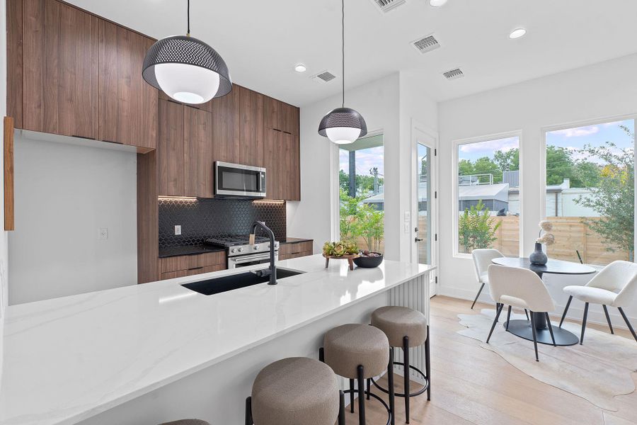 Kitchen with modern cabinets, stainless steel microwave, brown cabinetry, a breakfast bar area, and recessed lighting