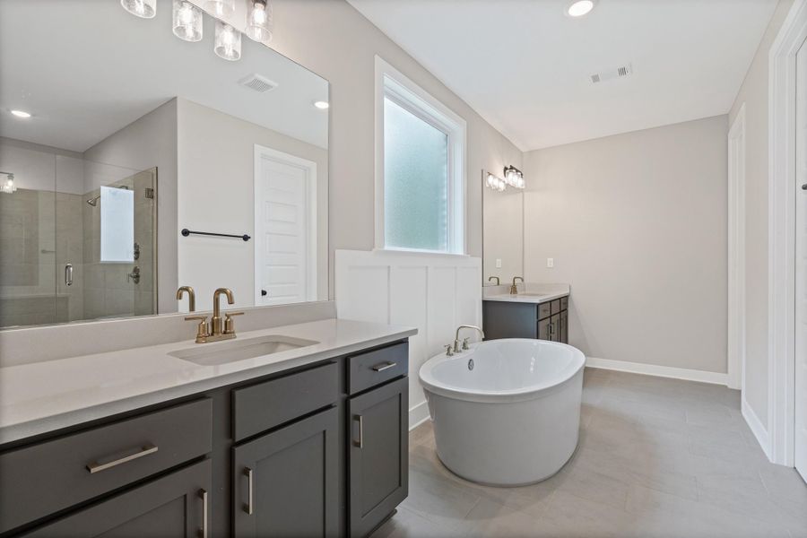 Freestanding soaking tub with brushed brass fixtures, complemented by dual vanities with quartz countertops and dark cabinetry Freestanding soaking tub with brushed brass fixtures, complemented by dual vanities with quartz countertops and dark cabinetry