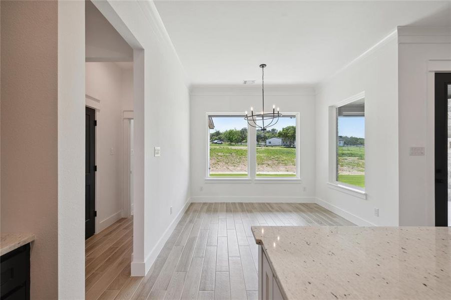 Unfurnished dining area featuring light wood-type flooring, crown molding, and a notable chandelier