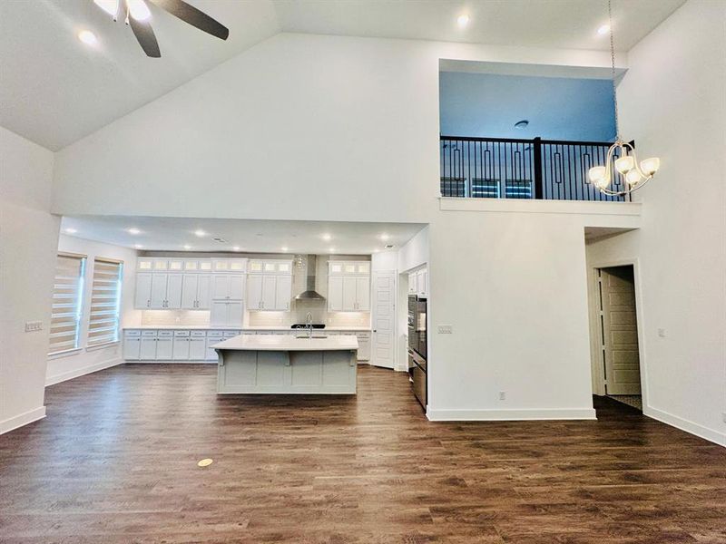 Kitchen with high vaulted ceiling, wall chimney range hood, and a center island with sink