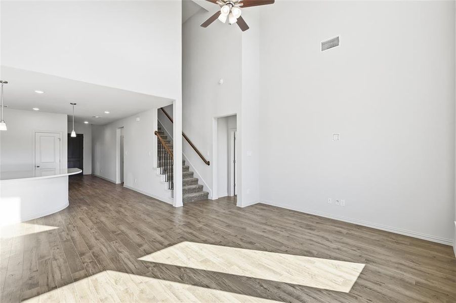 Unfurnished living room featuring light wood-style floors, recessed lighting, stairway, a ceiling fan, and a towering ceiling