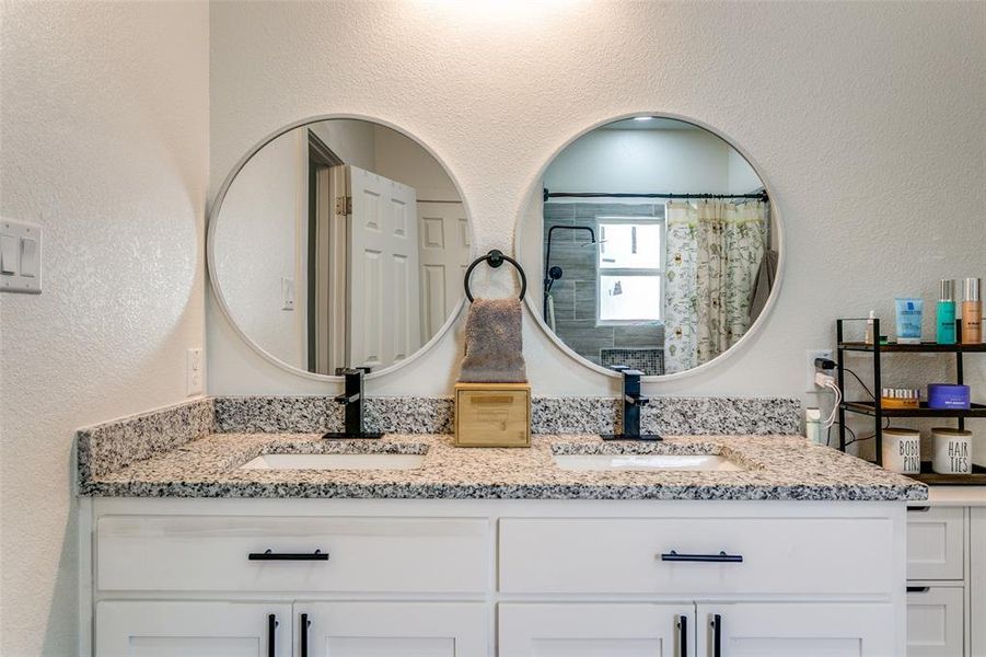 Bathroom featuring a textured wall, double vanity, and curtained shower Bathroom featuring a textured wall, double vanity, and curtained shower