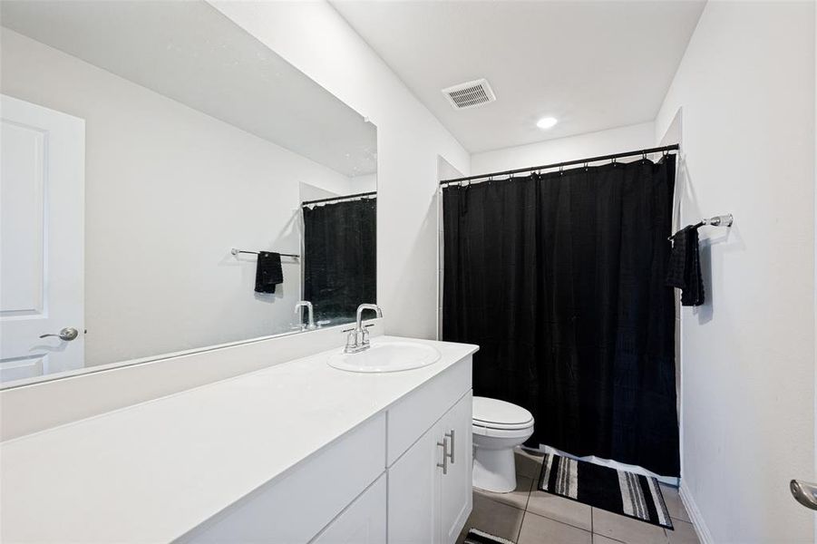 Bathroom featuring a single vanity with an integrated sink, a large wall-mounted mirror, white cabinetry with silver-tone hardware, and a shower-tub combination behind a black curtain Bathroom featuring a single vanity with an integrated sink, a large wall-mounted mirror, white cabinetry with silver-tone hardware, and a shower-tub combination behind a black curtain