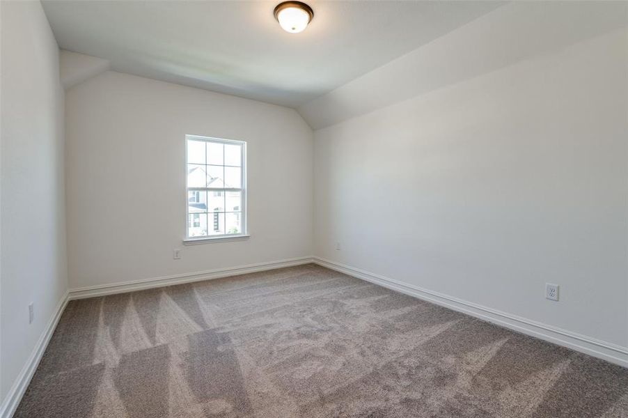 Carpeted spare room featuring vaulted ceiling