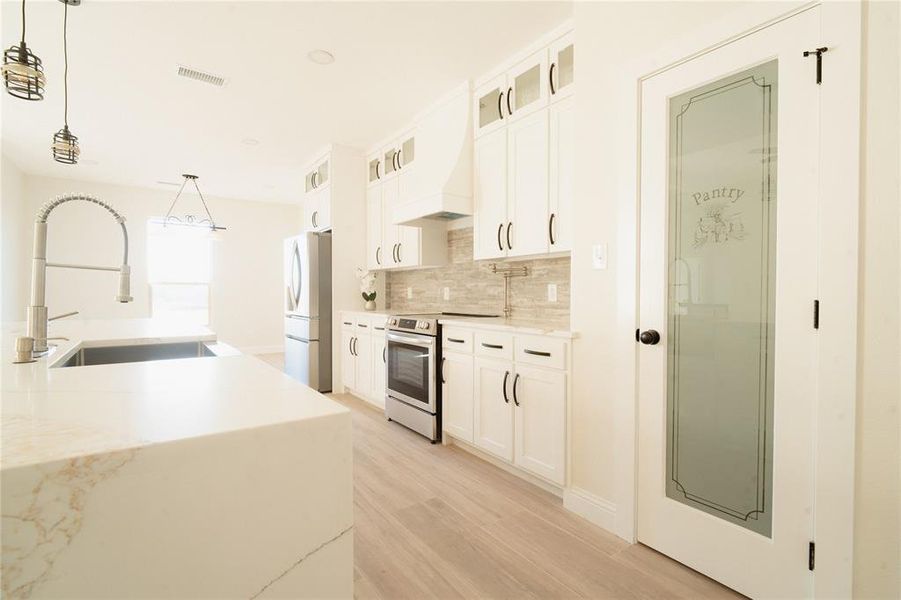 Kitchen featuring premium range hood, a sink, visible vents, stainless steel range with electric cooktop, and freestanding refrigerator