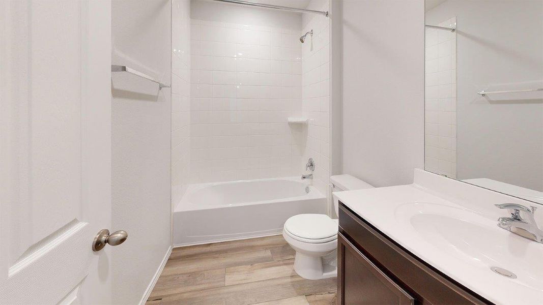 Bathroom featuring a white subway tile tub surround, wood-finish flooring, a dark wood vanity with white countertop, and a large mirror Bathroom featuring a white subway tile tub surround, wood-finish flooring, a dark wood vanity with white countertop, and a large mirror