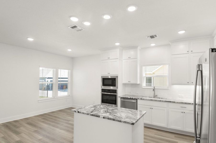 Kitchen with stainless steel appliances, decorative backsplash, light wood finished floors, light stone countertops, and a kitchen island Kitchen with stainless steel appliances, decorative backsplash, light wood finished floors, light stone countertops, and a kitchen island