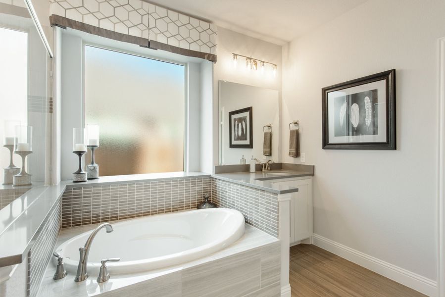 Master bathroom with soaking tub, gray tile surround, white vanity, and frosted window