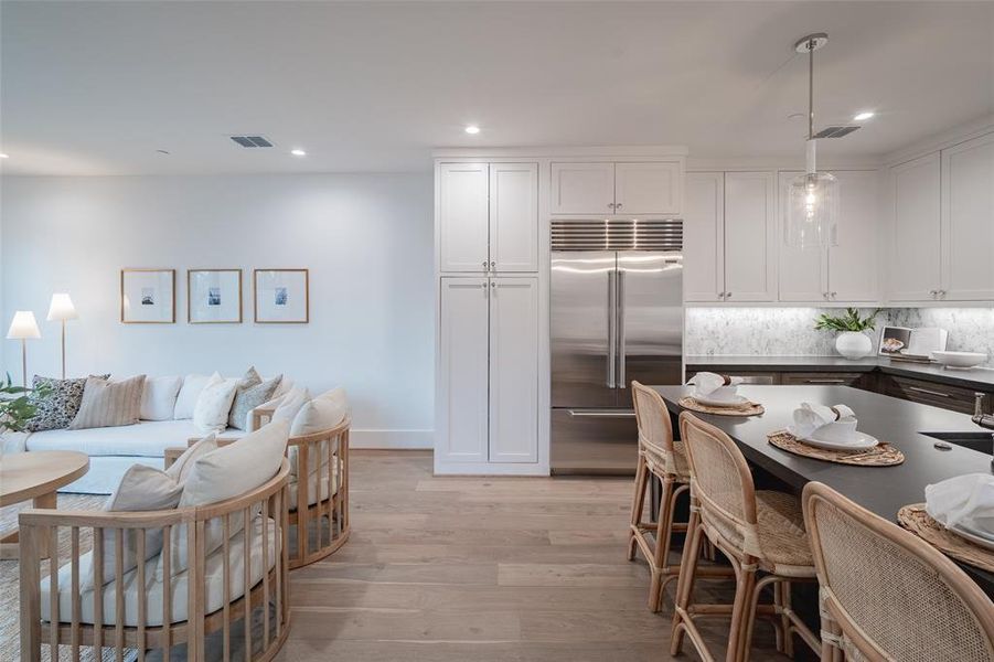 Kitchen featuring tasteful backsplash, white cabinets, hanging light fixtures, stainless steel built in fridge, and light hardwood / wood-style floors