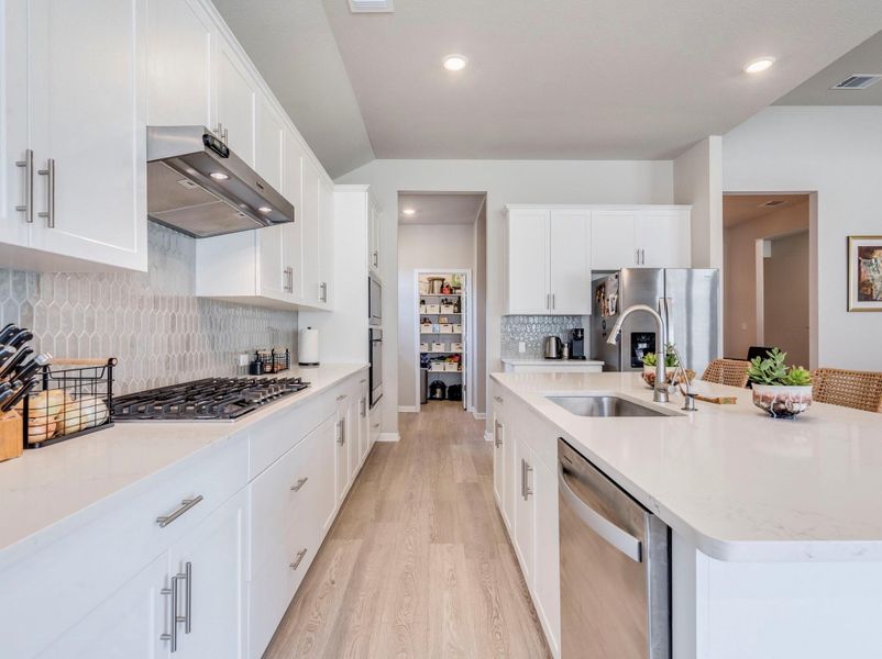 Built in gas range and exhaust vent elevate this modern chef's kitchen, featuring a central island with sink.