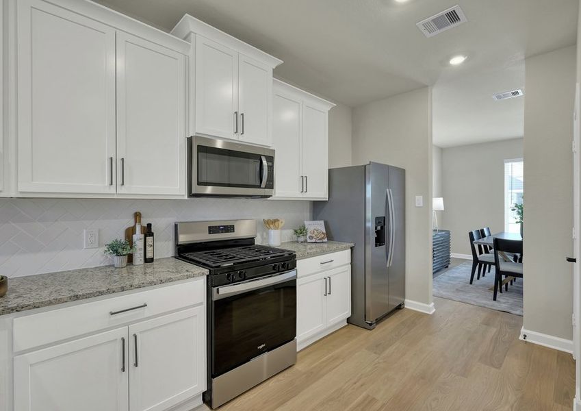 Kitchen featuring a stainless steel gas range, microwave, and refrigerator with granite countertops and white cabinetry.