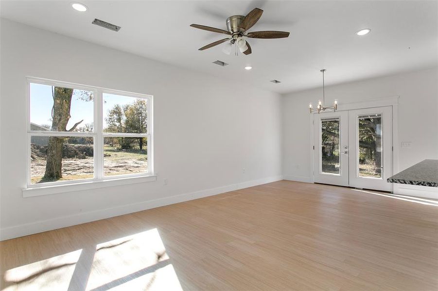 Spare room with ceiling fan with notable chandelier, a healthy amount of sunlight, french doors, and light hardwood / wood-style flooring