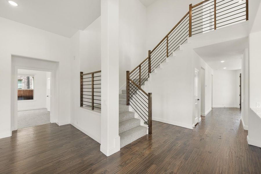 Open foyer with two-story ceiling, staircase with metal railing, and dark hardwood floors