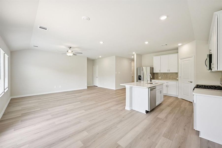 Kitchen featuring white cabinetry, a ceiling fan, a kitchen island with sink, open floor plan, and stainless steel appliances