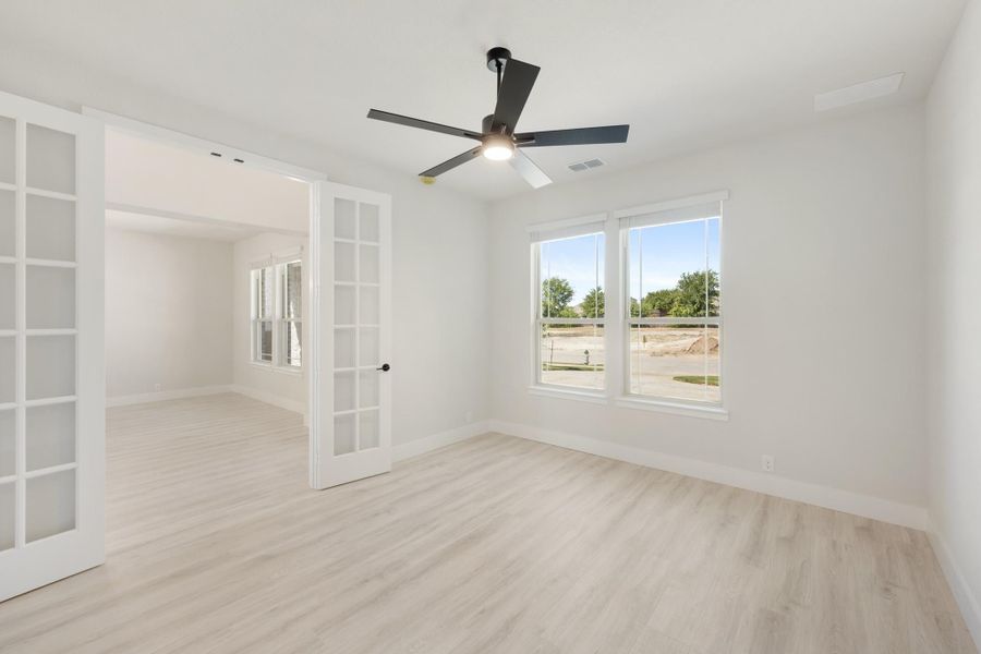 Empty room with light wood floors, ceiling fan, and white French doors leading to adjacent room