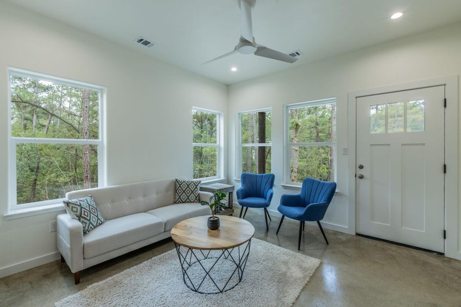 Light-filled living area featuring multiple windows, a white paneled entry door with glass inserts, recessed lighting, a ceiling fan, and concrete flooring Light-filled living area featuring multiple windows, a white paneled entry door with glass inserts, recessed lighting, a ceiling fan, and concrete flooring
