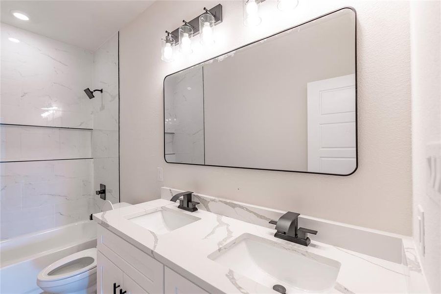 Full bathroom featuring tiled shower / bath, dual bowl vanity, and toilet