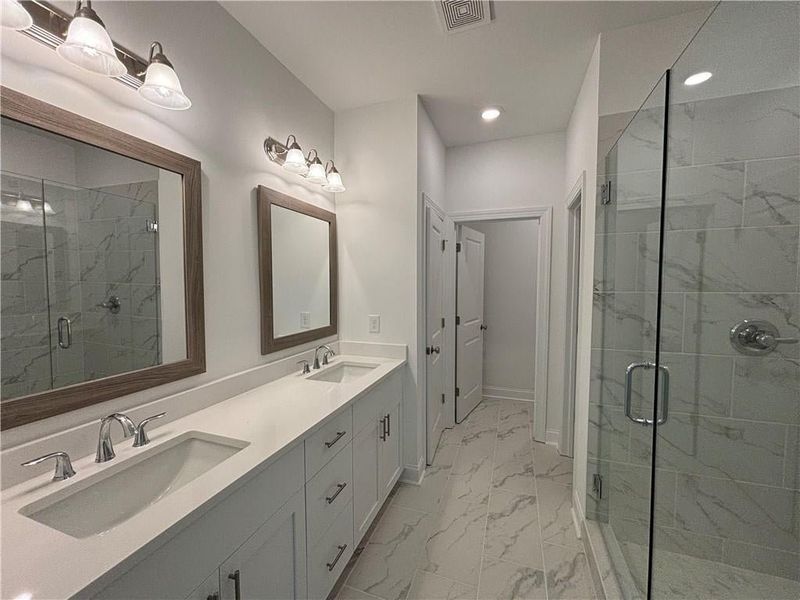 Primary bathroom has double vanities, large glass enclosed shower with custom tile.