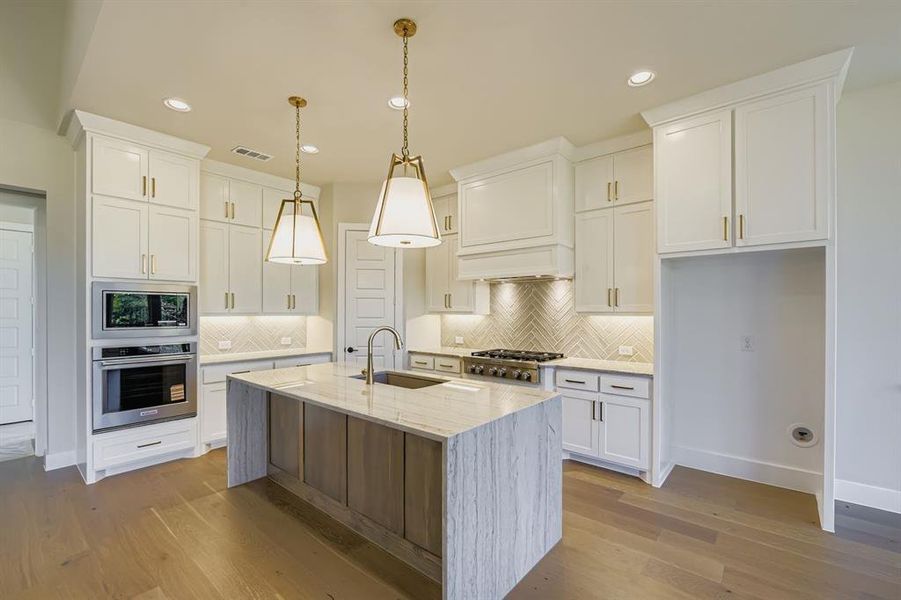 Kitchen with light stone counters, stainless steel appliances, decorative light fixtures, light wood-type flooring, and white cabinetry