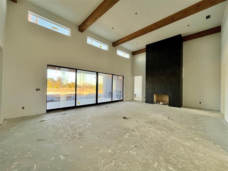 Unfurnished living room with a towering ceiling, beamed ceiling, and a healthy amount of sunlight