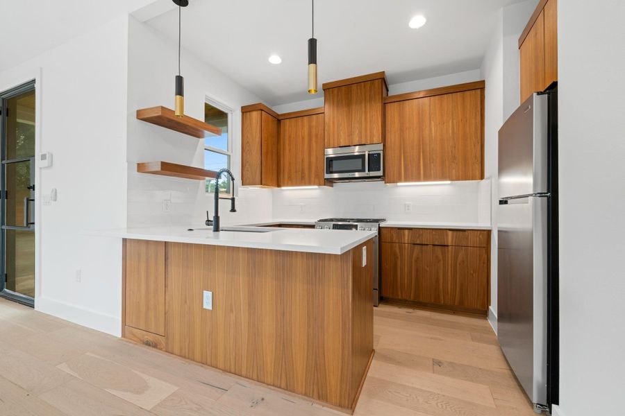 Kitchen with appliances with stainless steel finishes, brown cabinets, open shelves, a peninsula, and tasteful backsplash Kitchen with appliances with stainless steel finishes, brown cabinets, open shelves, a peninsula, and tasteful backsplash