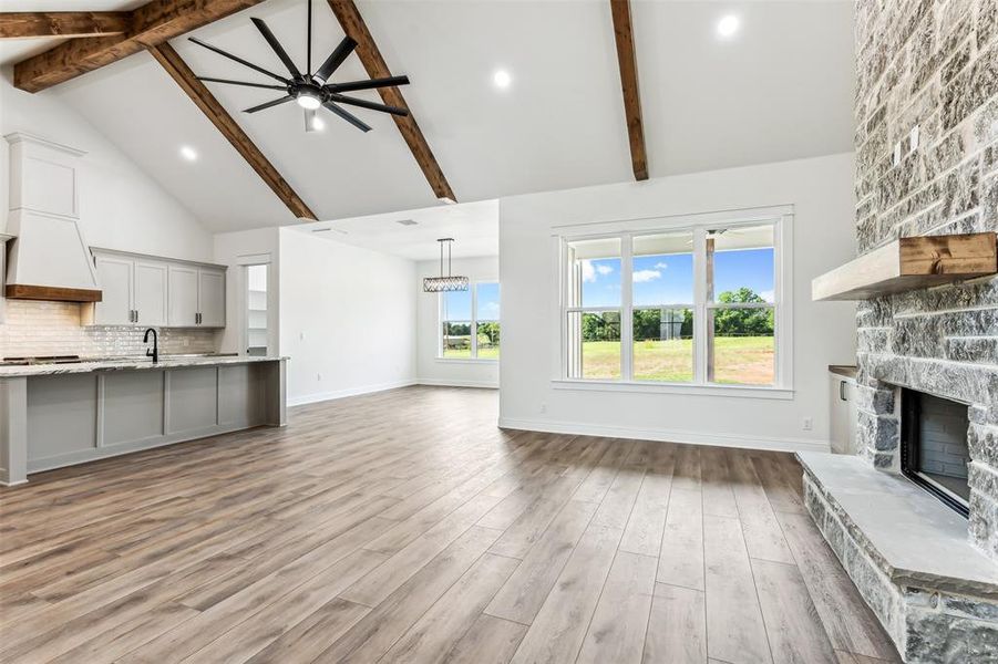 Living room featuring beam ceiling, light hardwood / wood-style flooring, ceiling fan, a stone fireplace, and high vaulted ceiling