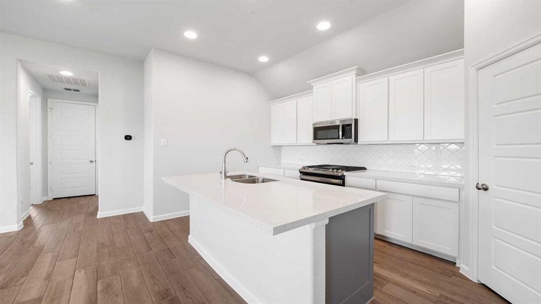 Kitchen with tasteful backsplash, hardwood / wood-style flooring, sink, a center island with sink, and appliances with stainless steel finishes